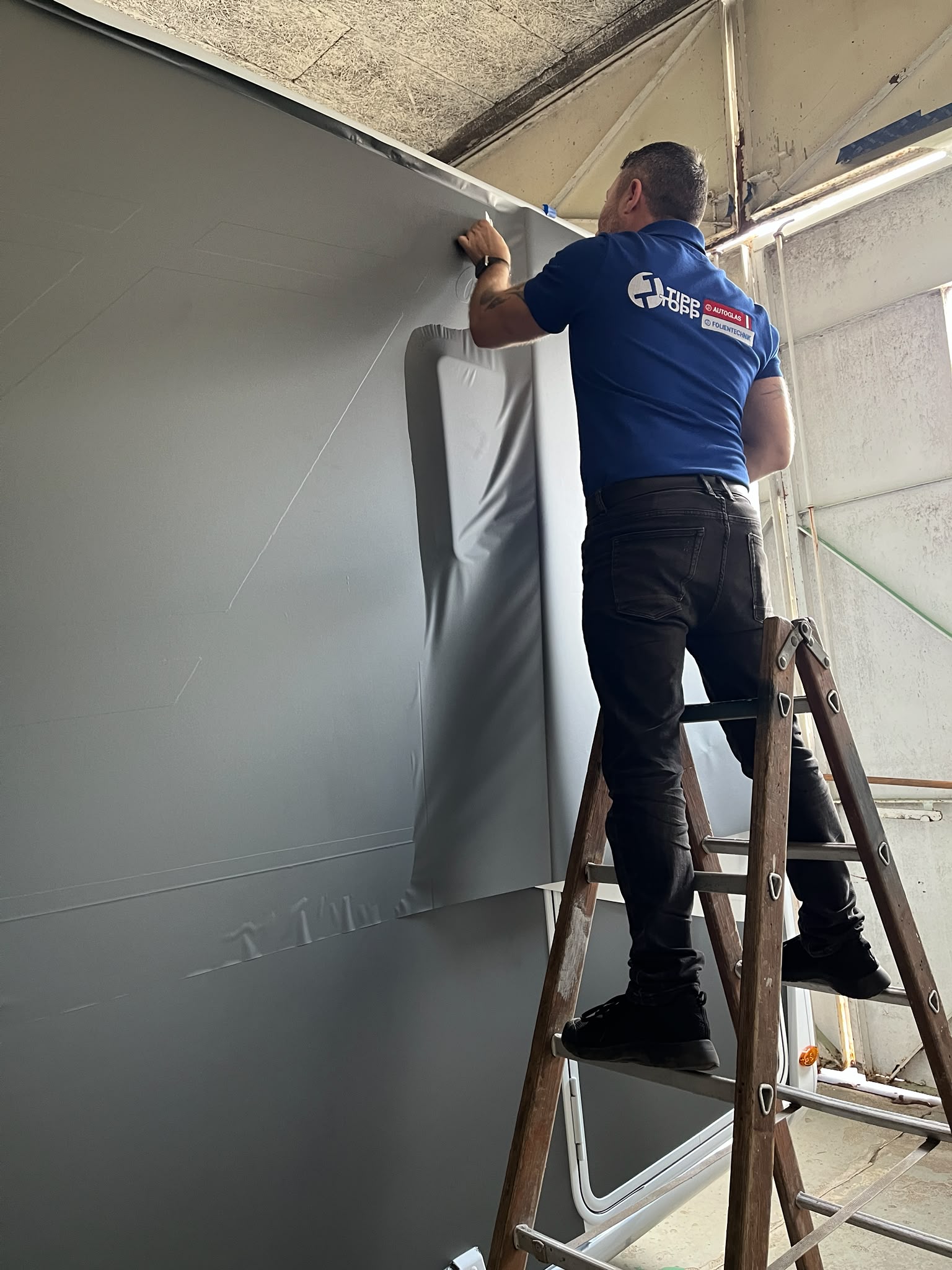 Wadim Meier bei der präzisen Großflächen-Folierung einer Wand in der Werkstatt von Tipp Topp Autoglas & Folientechnik in Stade